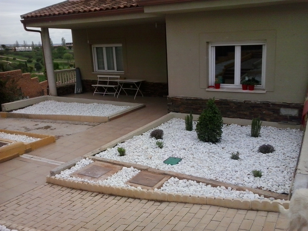 Jardín de bajo mantenimiento con grava blanca y arbustos frente a una vivienda